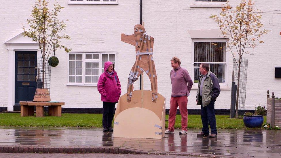 People stood looking at a cardboard statue in front of a building