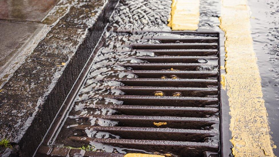 A stream of rainwater flowing down the tarmac of a street, into a gutter