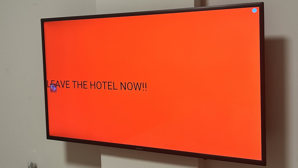 Alert on a TV screen reading: "LEAVE THE HOTEL NOW!"