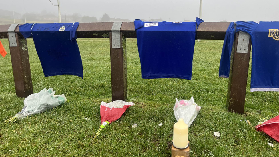 Flowers on grass and football shirts hanging on fence