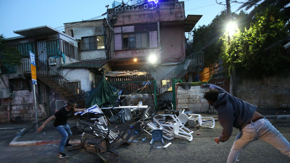 Two men throwing chairs at a house flying the Israeli flag in Sheikh Jarrah