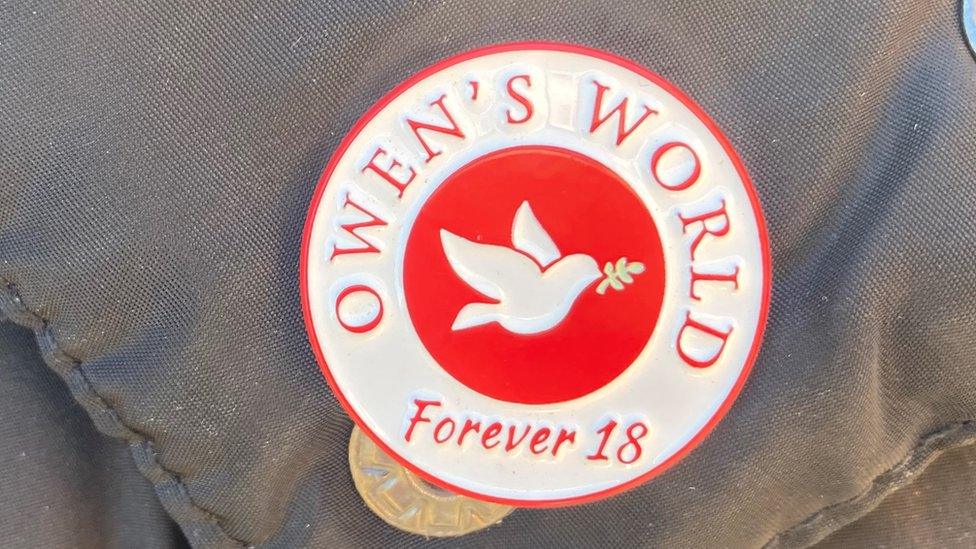 A red and white pin with a dove in the centre, Owen's World at the top and forever 18 underneath the logo of the community interest company set up in Mr Dunn's memory