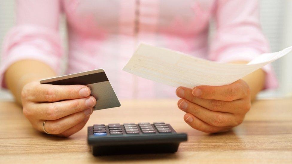 Woman holding bank card and paper above calculator