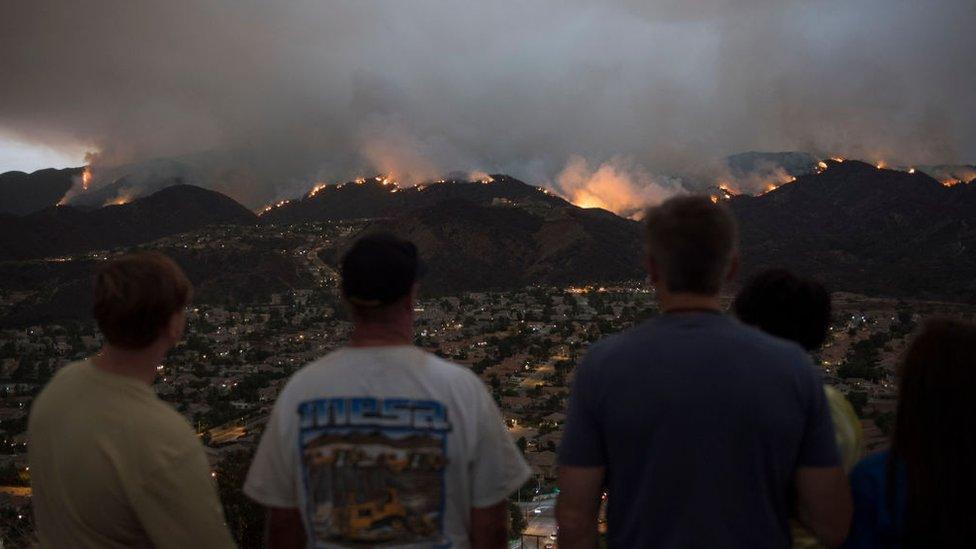 Evacuees watch the flames crest over the nearby mountains