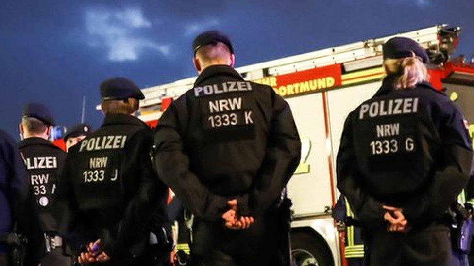 The backs of five police officers, in front of fire engines