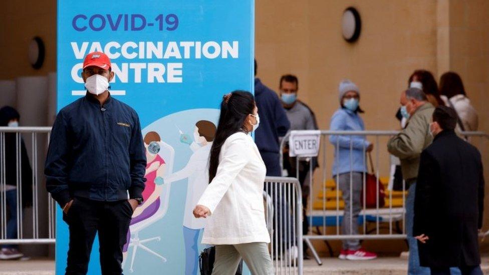 People wearing protective masks queue for booster injections of a coronavirus disease