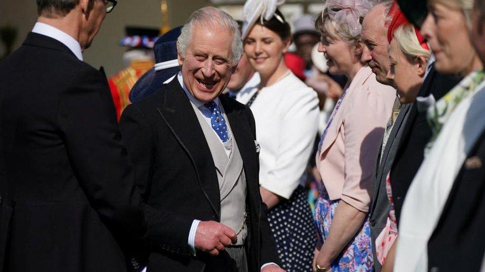 King Charles smiles as he meets guests at Buckingham Palace