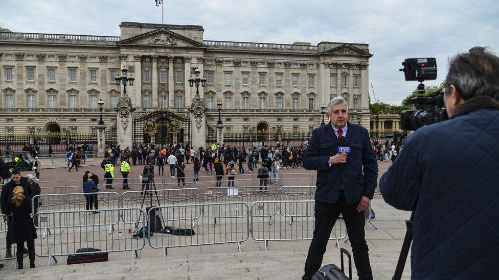 A news broadcaster speaks to camera as members of the public queue to read the official notice of the birth of a baby boy to the Duke and Duchess of Sussex outside Buckingham Palace on May 6, 2019