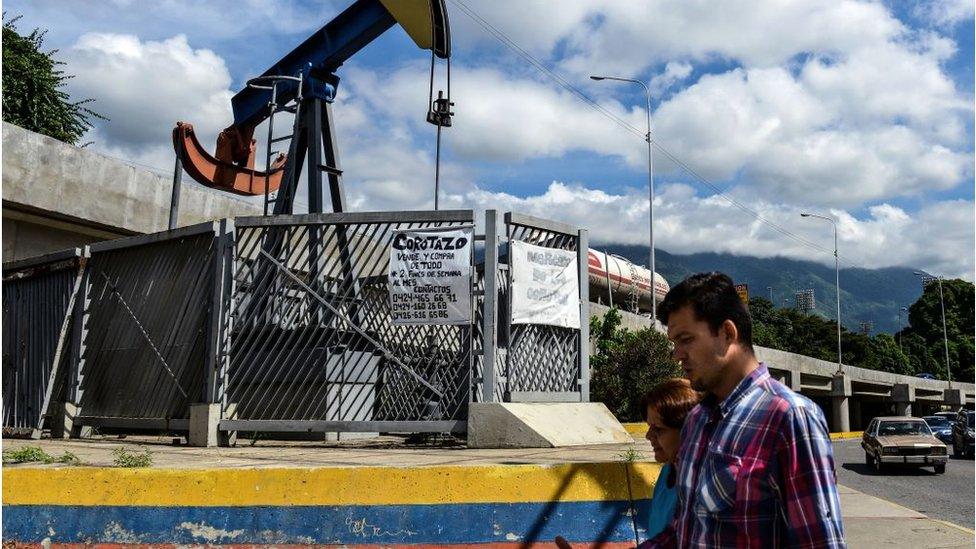 People walk by a small square with an oil pump