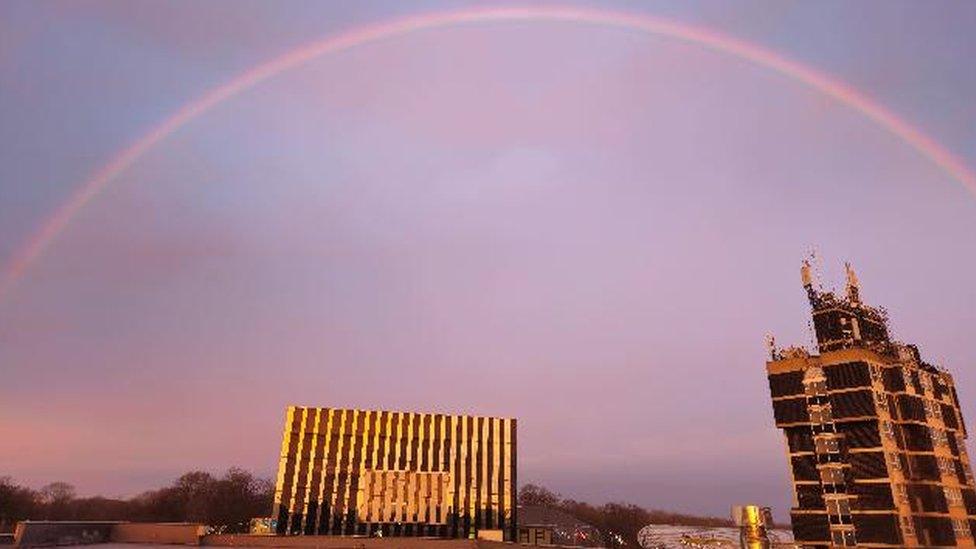 Rainbow against blue and pink sky with concrete buildings beneath