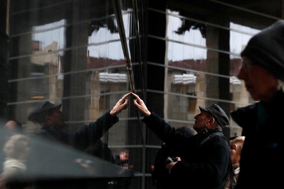 A man touches a wall bearing the names of victims