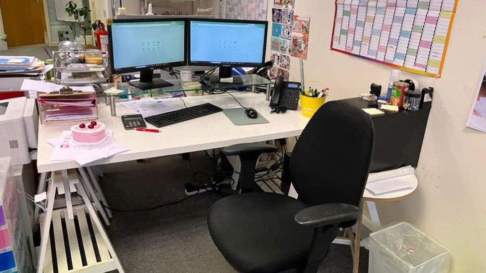 A desk with two computer monitors, a black chair and a pink cake