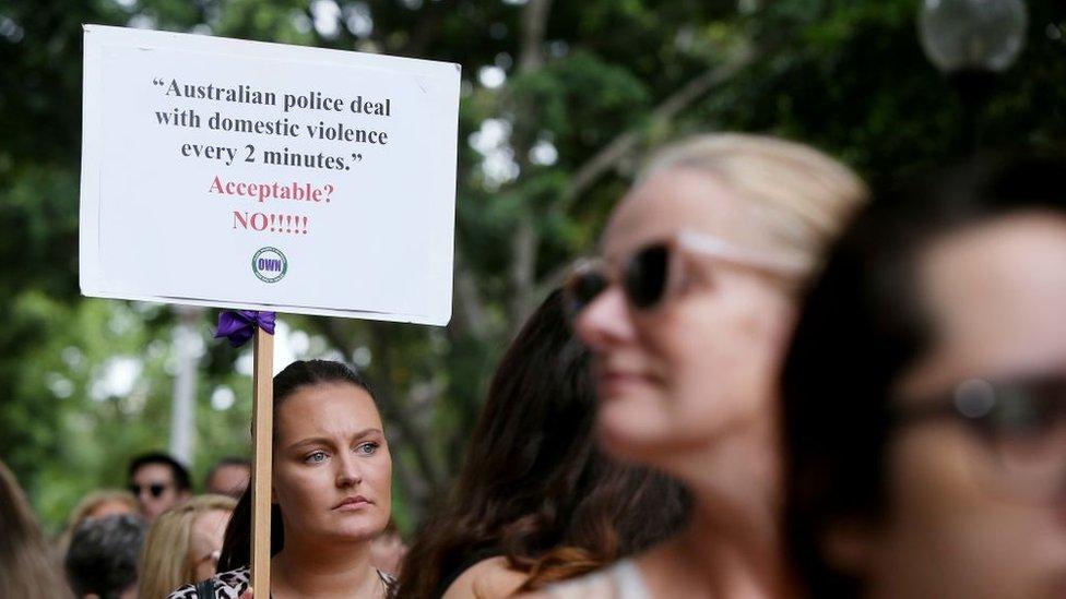 A woman at a women's march holding a sign that says police respond to a domestic violence call every two minutes