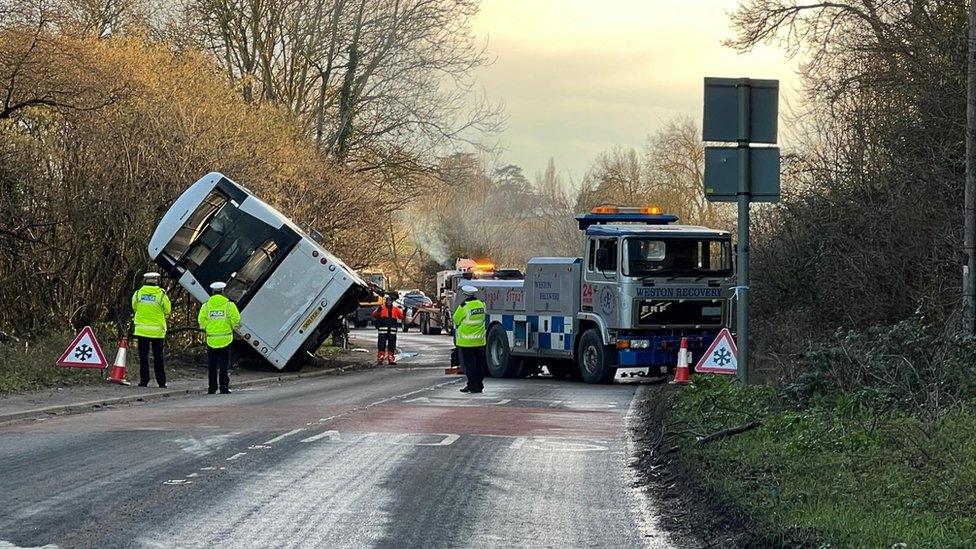 Double-decker leaning against a hedge, wheels in the air