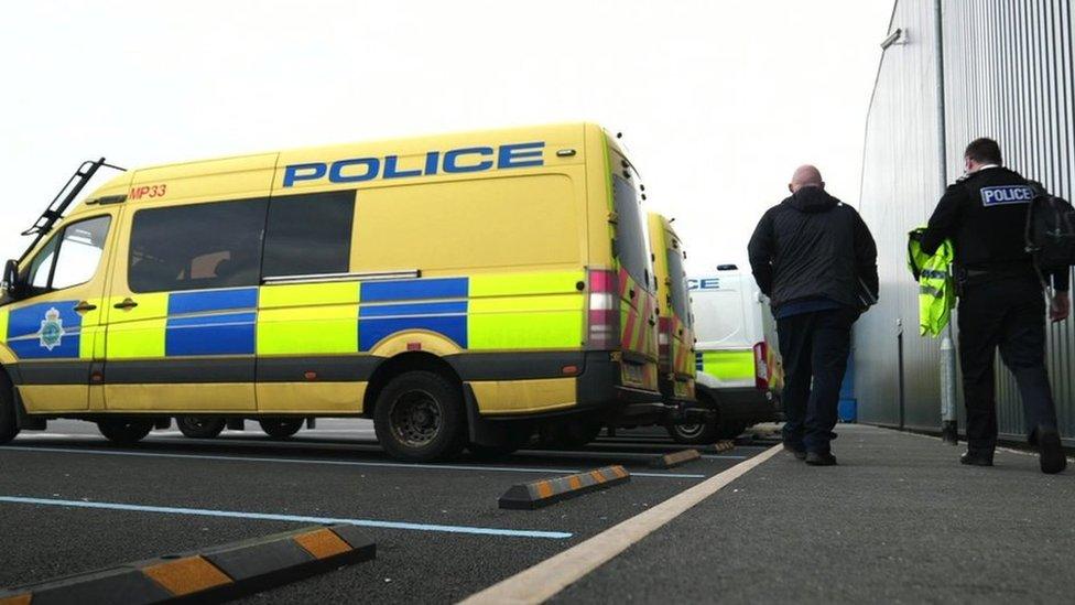 Two men walk behind a police van