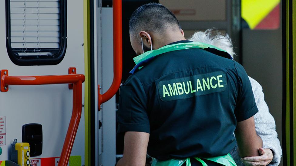 A paramedic helps an elderly woman step down from an ambulance outside the emergency department of the Royal London Hospital in London, England, on January 25, 2021