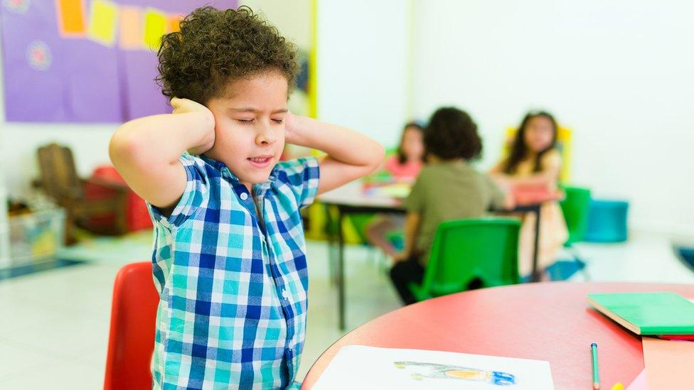 Stock photo of young boy covering his ears in a classroom