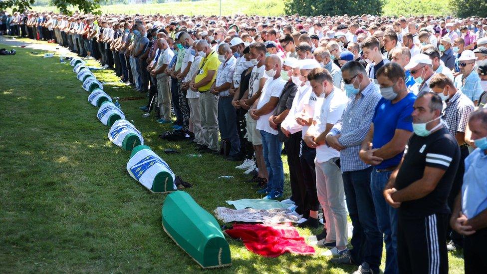 People pray near coffins at a graveyard during a mass funeral in Potocari