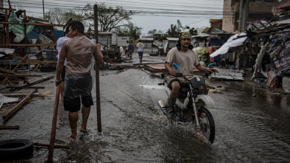 Residents drive through flooded streets with debris