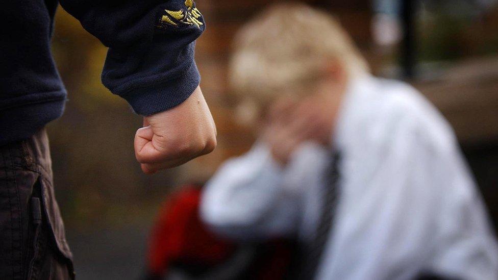 A bully clenches his fist while his victim is seen in the background