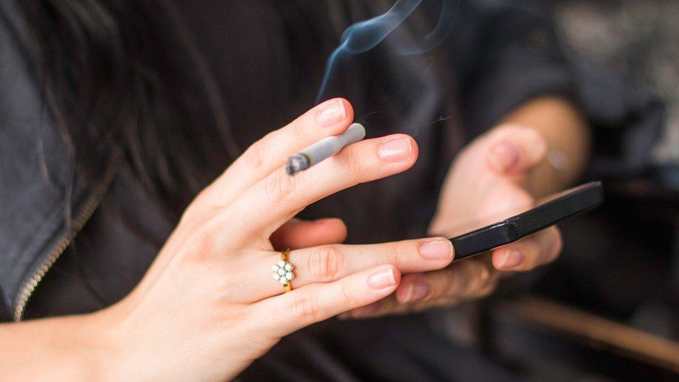 hands holding a cigarette and a smartphone