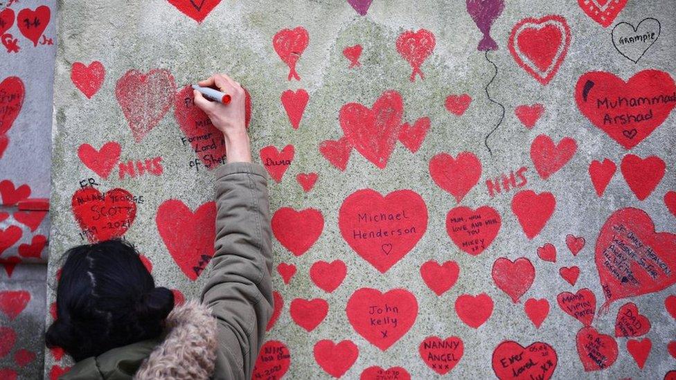 A person paints on the National Covid Memorial wall beside St Thomas" hospital set as a memorial to all those who have died so far in the UK from the coronavirus disease (COVID-19), amid the coronavirus pandemic in London