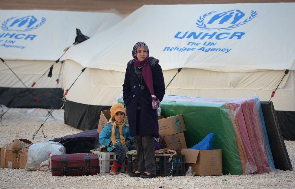 Refugees stand with a few possessions in a refugee camp in Jordan