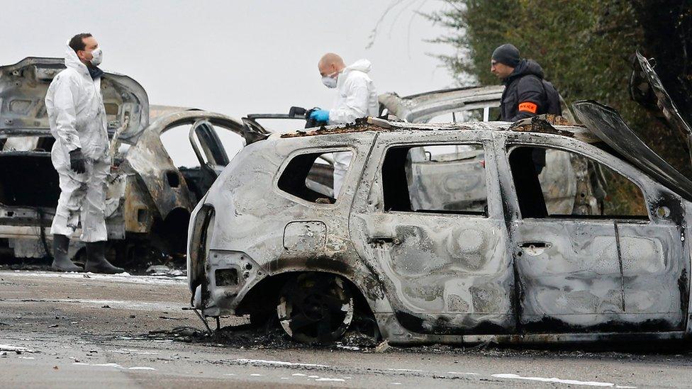 French police officers search through the burnt-out cars