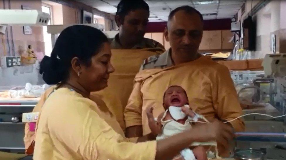 A nurse feeds the baby at the hospital as policemen look on