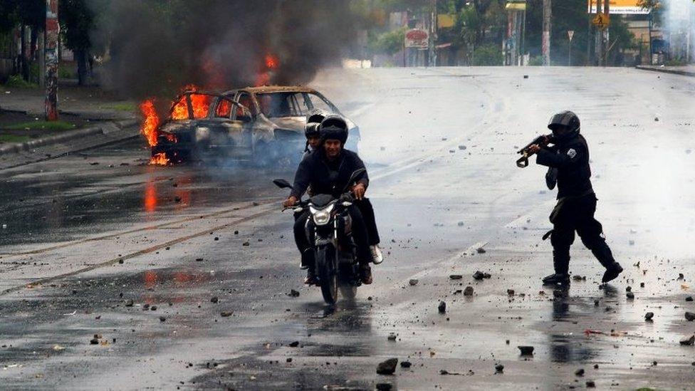 A riot police officer fires his shotgun towards two men during a protest against Nicaragua's President Daniel Ortega's government in Managua, Nicaragua May 28