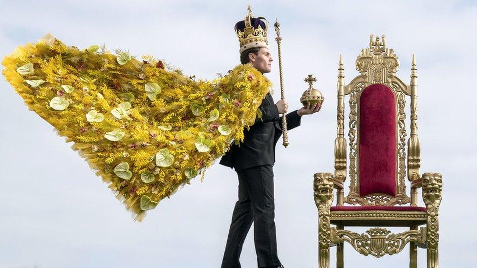 Model wearing robe made of flowers, a replica crown and holding a sceptre and orb