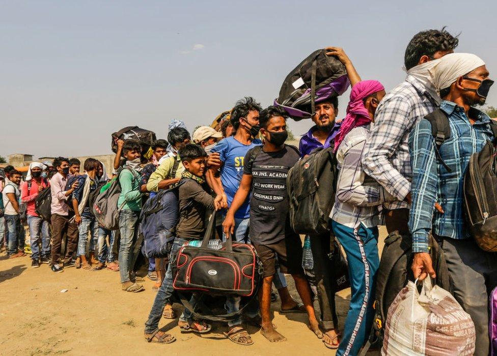 Migrant workers with their families queue up waiting to board buses back home.