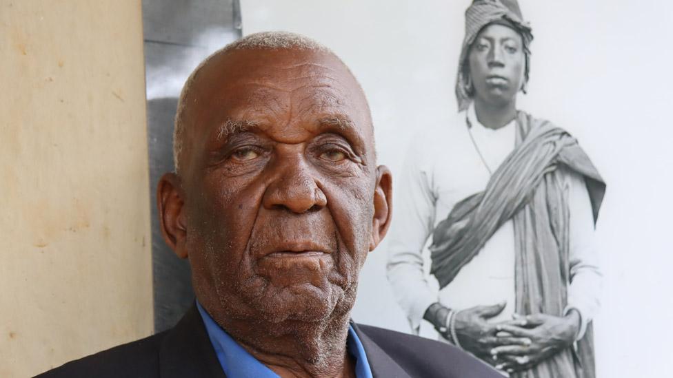 Isaria Meli standing next to a portrait of his grandfather