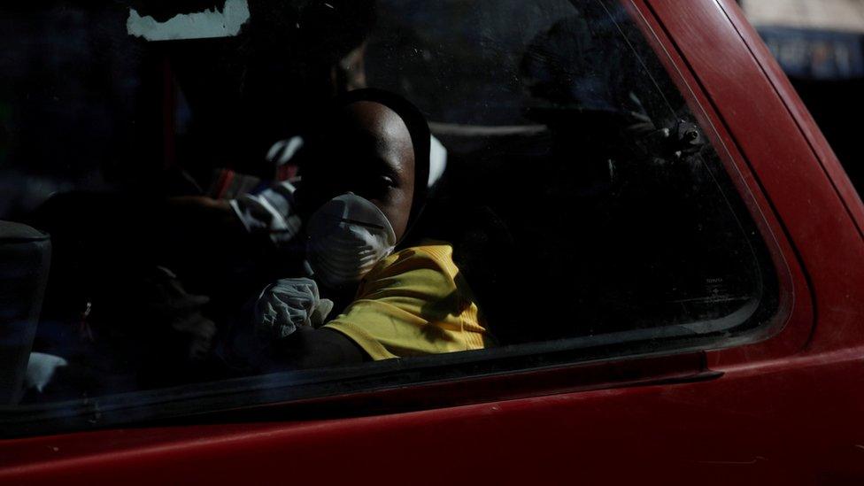 A boy wearing protective gloves and a mask travels in a van, after Haiti"s government declared a state of emergency