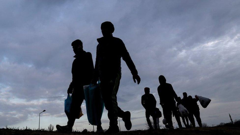 A silhouetted group of migrants and refugees