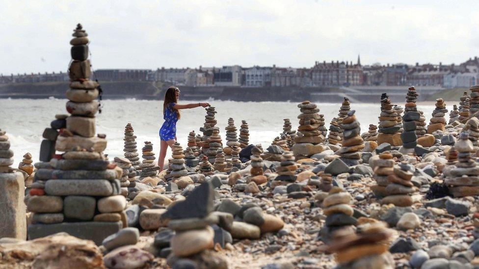 Girl adds pebbles to tower with Whitley Bay in distance