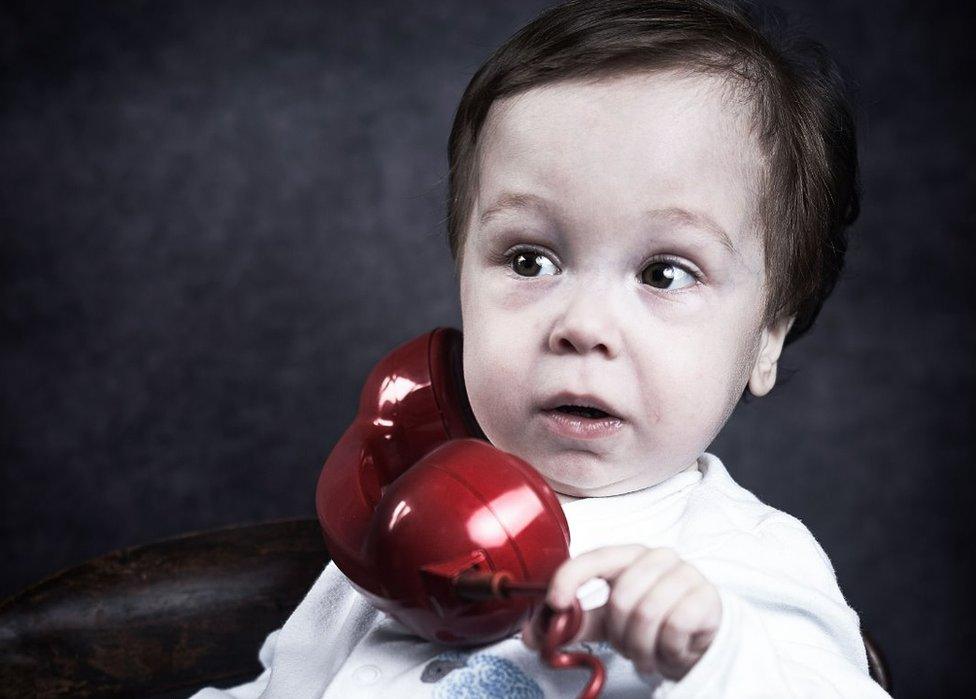 A young boy holds a phone up to his ear