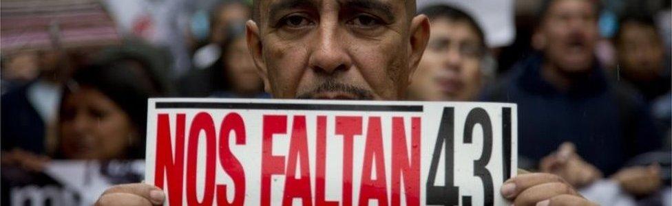 A man holds a sign that reads in Spanish: "We"re missing 43" during a march marking the one year anniversary of the disappearances of 43 college students in Mexico City on 26 September 2015