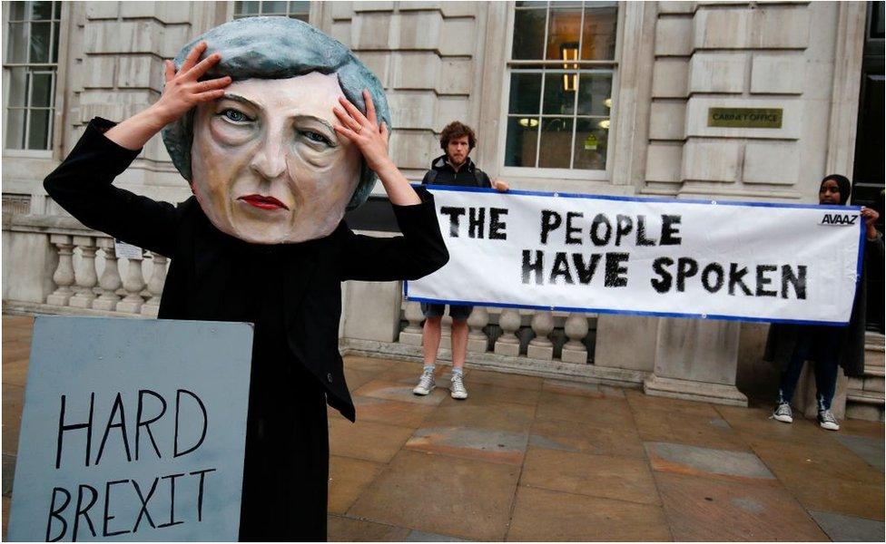 A demonstrator wears a mask depicting Theresa May