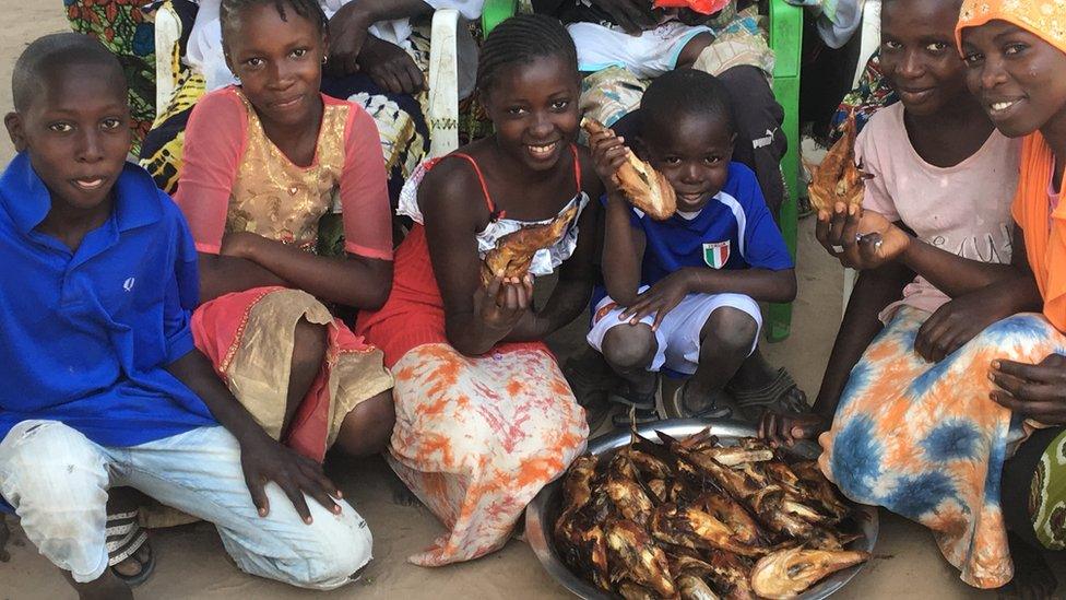 Young members of "Taka" Babucarr Bojang's family posing around a plate of fish