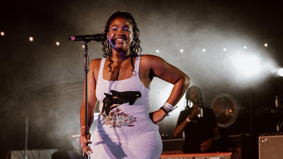 Debbie performs onstage, she's wearing a sequin lilac mini dress with a killer whale print. She's smiling, her hair is pulled back off her face, soft curls rest on her shoulders.