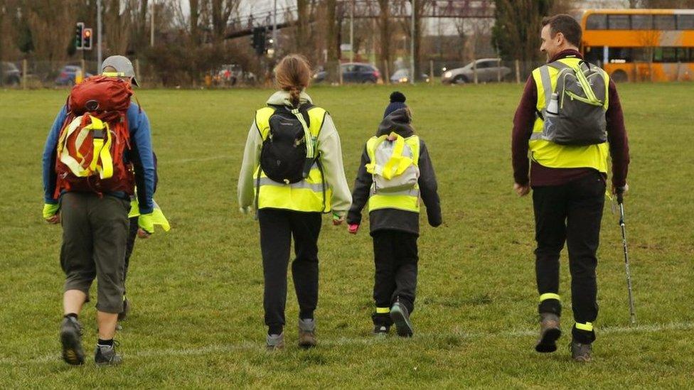 Four people walking while wearing high visibility jackets