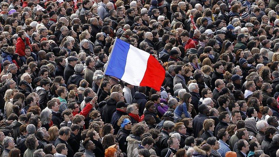 A man holds a French national flag in the middle of a large crowd