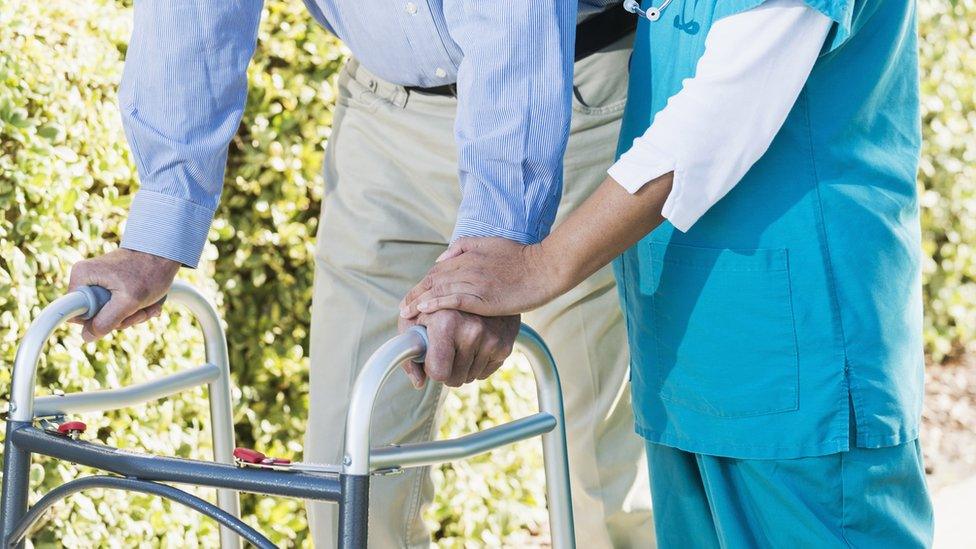 Carer supporting patient walking with a frame