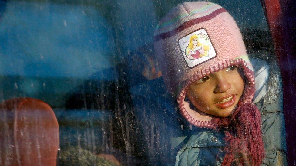 A migrant girl looking through a bus window in the makeshift refugee camp at the northern Greek border point of Idomeni, Greece, Friday, 25 March 2016.