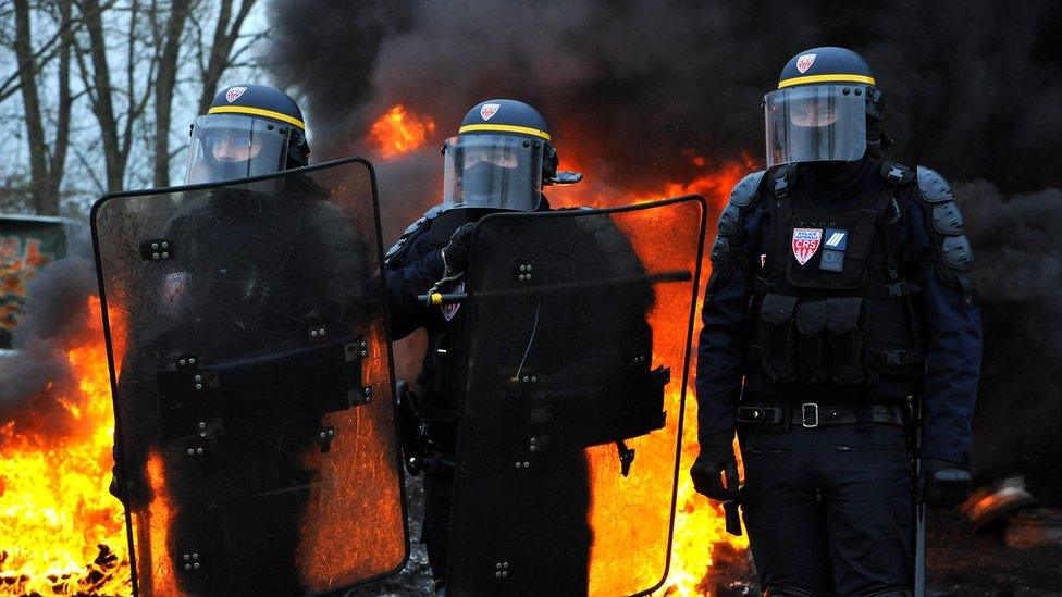 Riot police stand near a fire during a demonstration against rising fuel and oil prices in Crespin, northern France