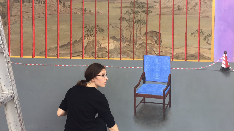 Marine Brossard painting a mural with a blue chair