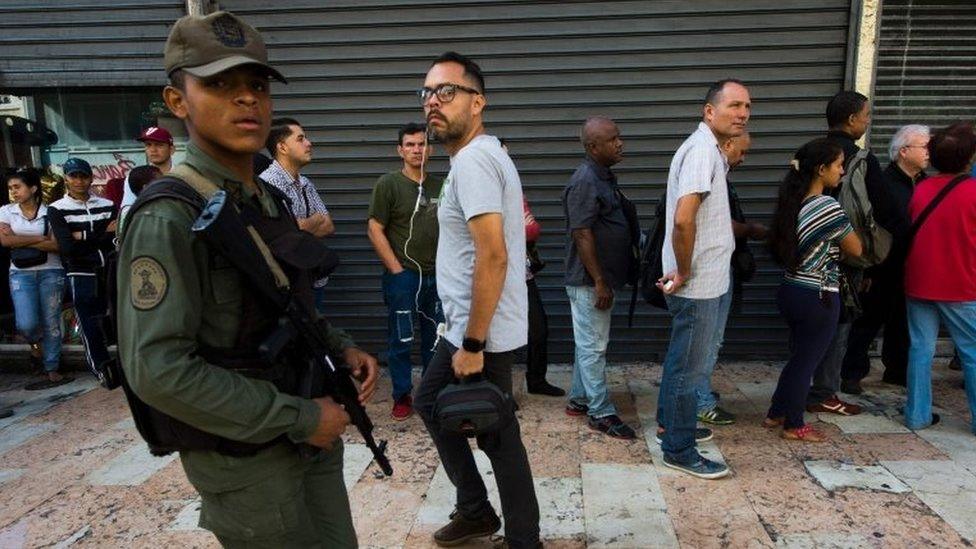 A Venezuelan soldier patrols as people queue outside a bank in Caracas in an attempt to deposit money, on 15 December 2016.