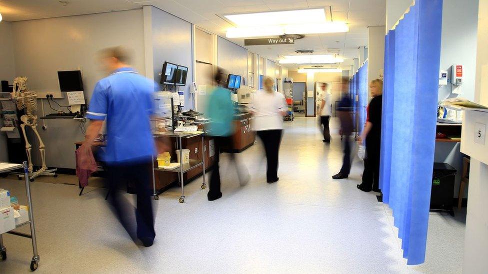 Staff in blue scrubs on a NHS hospital ward. They are slightly blurred because they are moving quickly