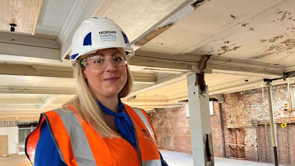 Natasha Hayes, the Executive Director of Place for the council, is inside the derelict building. She is wearing a white hard hat and an orange high visibility vest over a blue blouse. She also has on safety glasses.